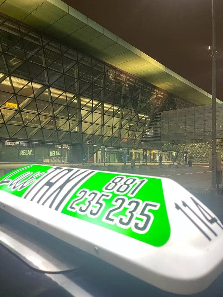 Kogut LUX Taxi przed terminalem lotniska nocą