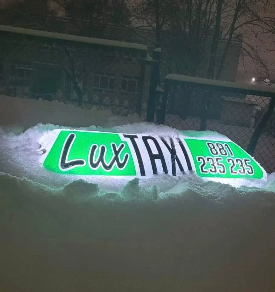 Podświetlony kogut LUX Taxi przysypany śniegiem nocą